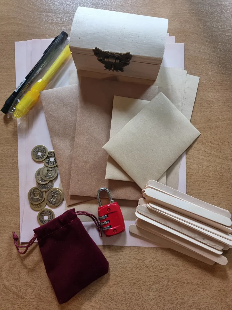 De inhoud van de box: een houten kistje, een cijferslot, munten, een rood zakje, pennen, oud papier, enveloppen en ijslollystokjes