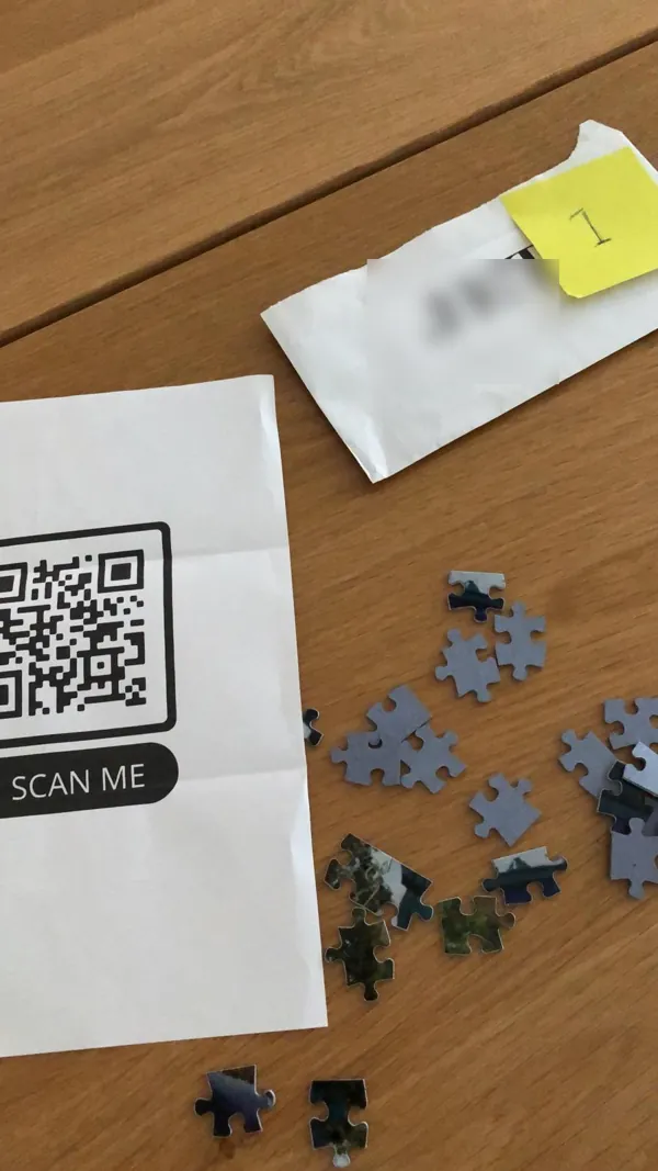 Een briefje met een QR-code, een genummerde envelop en losse puzzelstukjes op tafel