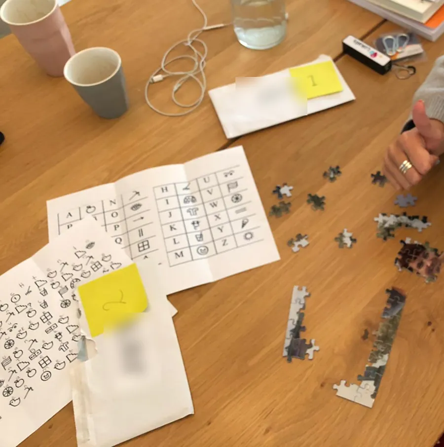 Een tafel met een geheimtaal-sleutel, genummerde enveloppen en een half gelegde legpuzzel